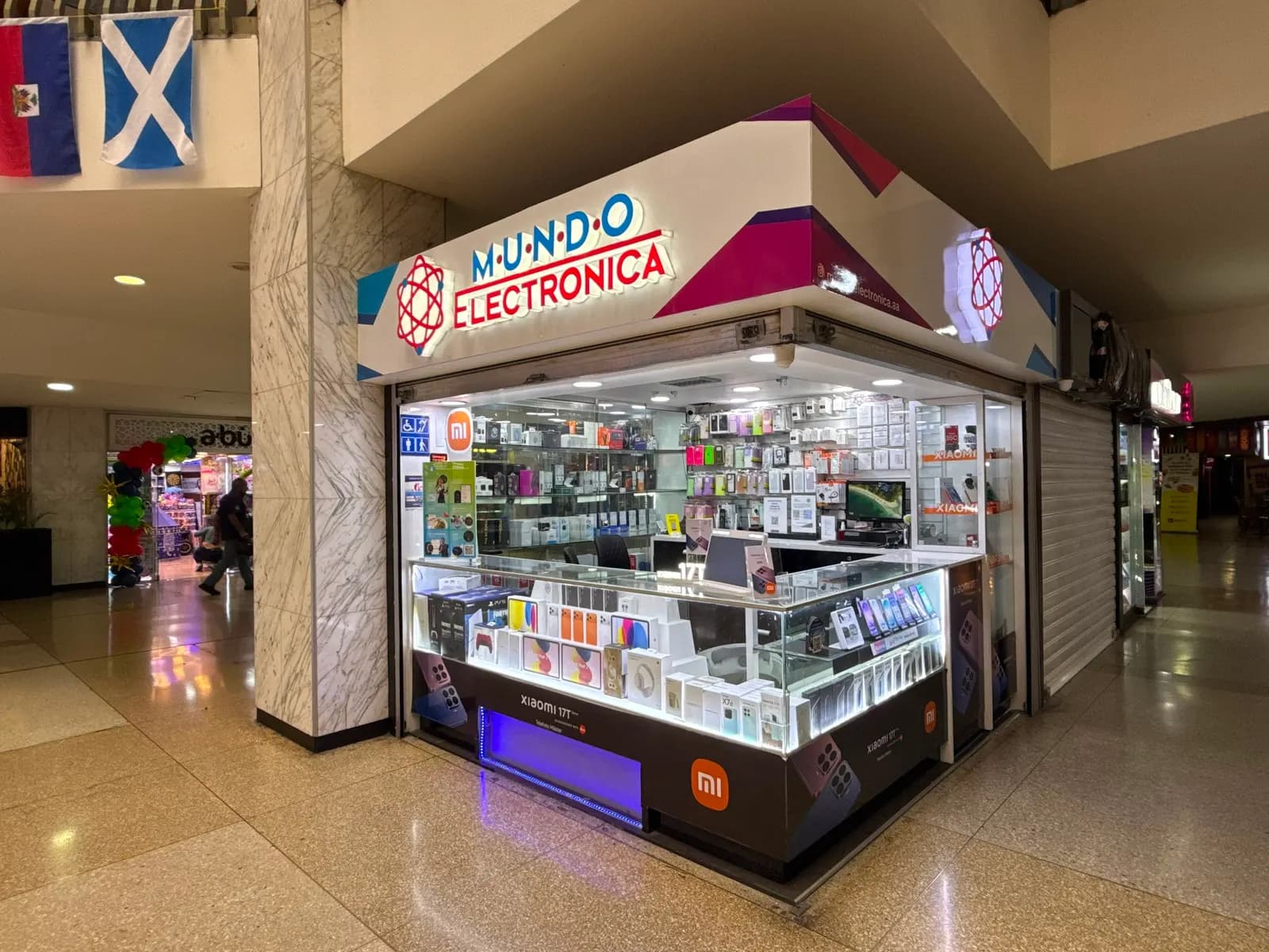 Vista en esquina del kiosco de Mundo Electrónica en el CCCT, con el aviso iluminado y las vitrinas de productos